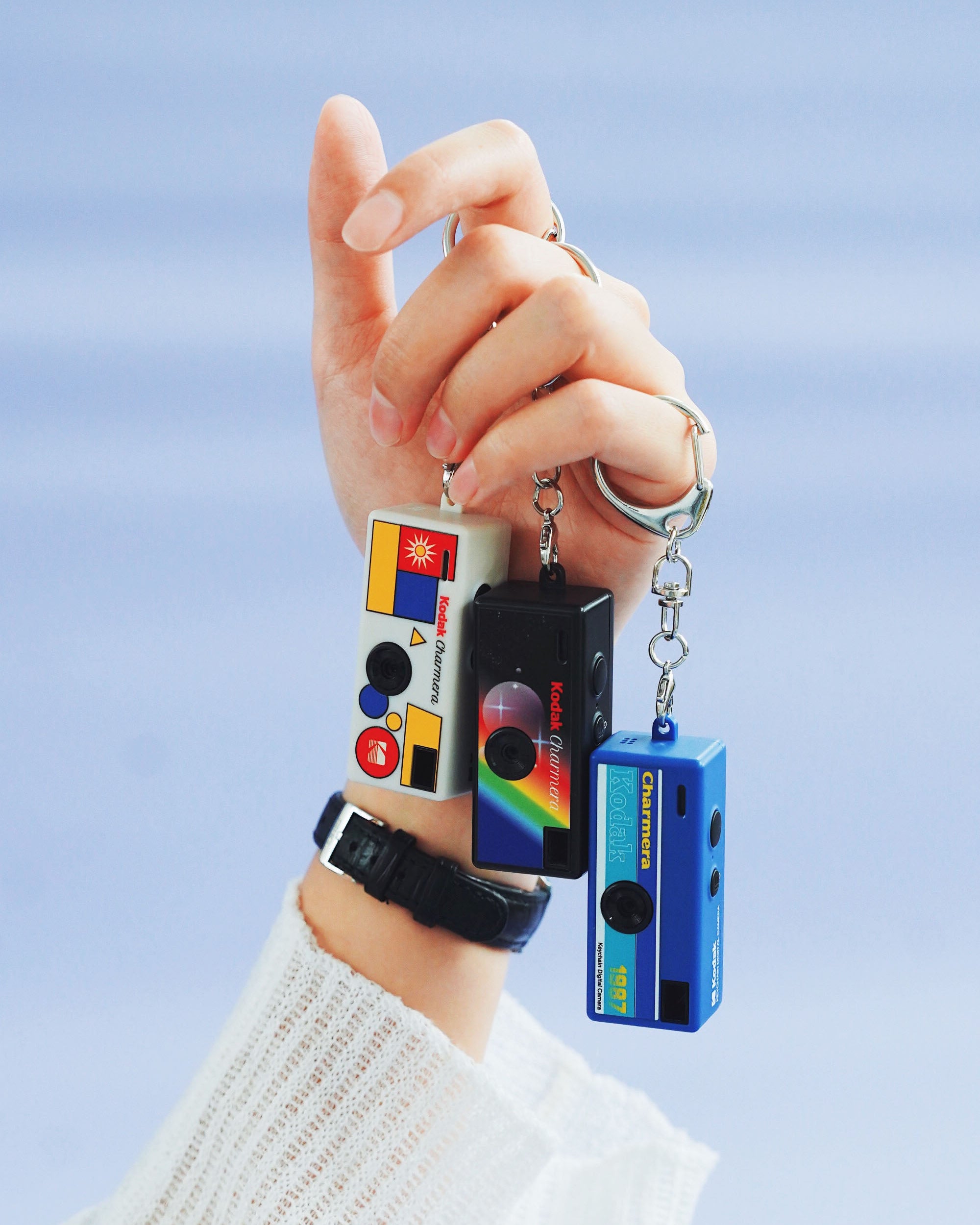 Hand holding a keychain with a retro-style radio and cassette player design against a light blue background.